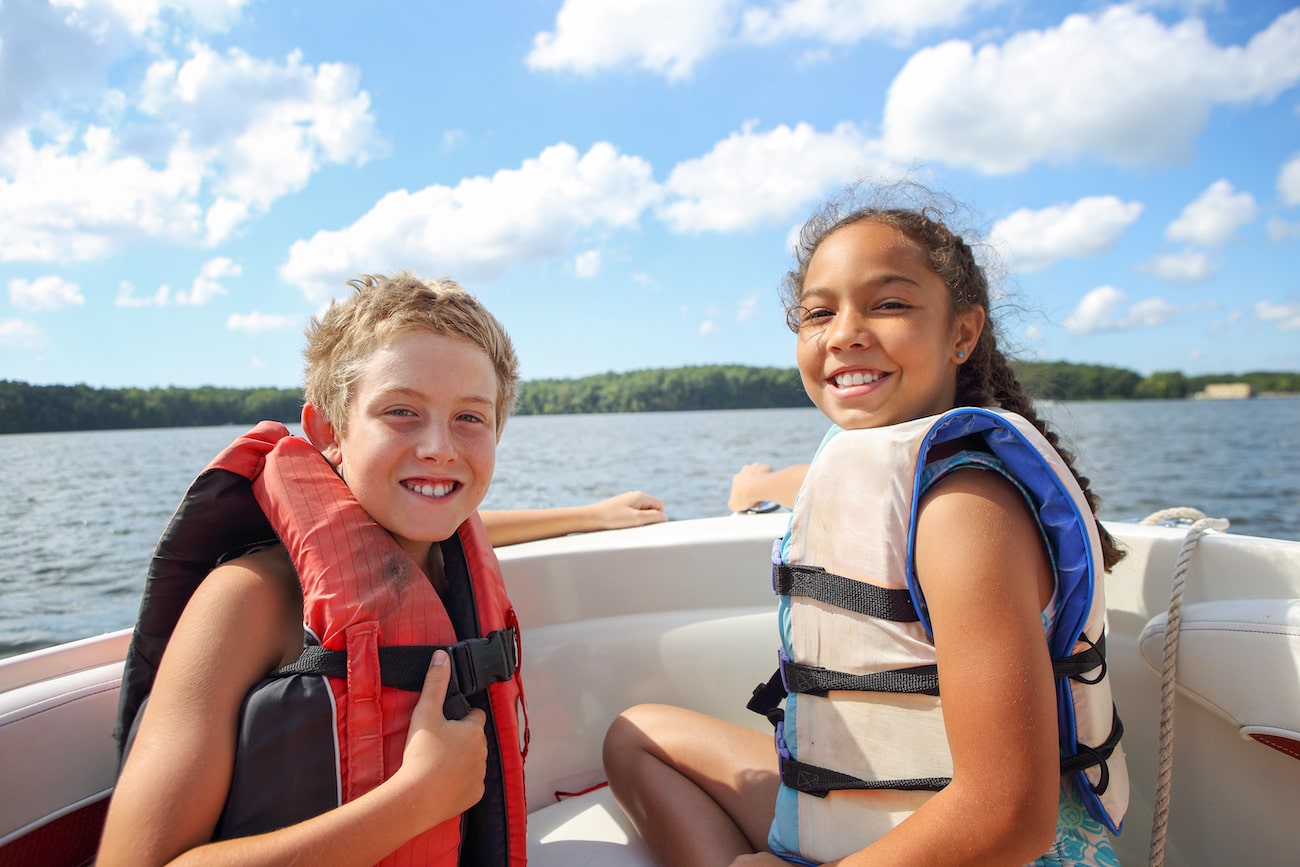 Two kids wearing life jackets on a ski boat